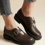 Brązowe skórzane półbuty damskie Vesta w stylu barefoot z szerokim noskiem i srebrną klamrą na grubszej podeszwie.